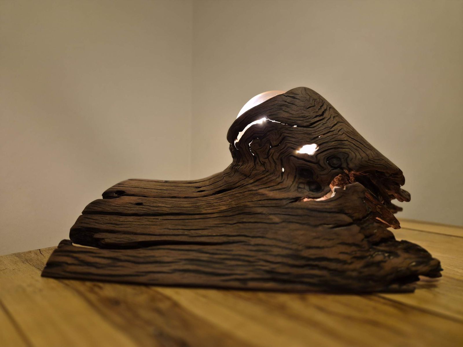 Dark weathered gum timber with rippling grain, lit from within as light escapes through cracks and holes