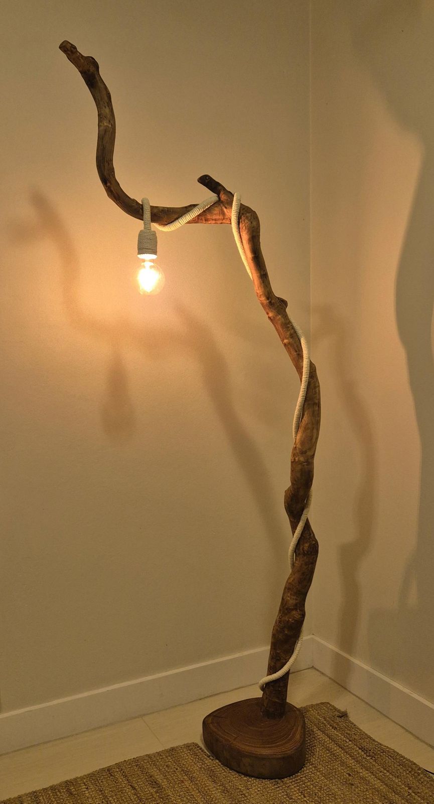 Two Fallen floor lamp: a curving gum branch on a round hardwood base, rope-wrapped cord ending in a hanging globe bulb